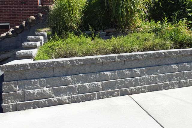 Custom stone retaining wall and granite steps engineered by A-Z Construction to manage drainage and soil erosion on a sloped Syracuse property.